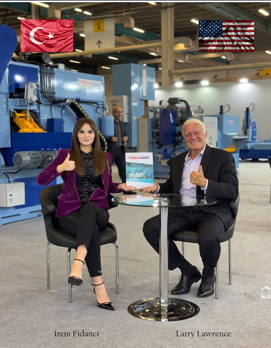 Larry Lawrence and Irem Fidanci seated at a Fimaksan trade show stand with sawmill machinery behind them
